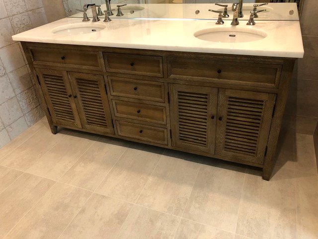 Dual-sink bathroom vanity with marble-look countertop and rustic oak cabinetry in Panama City Beach