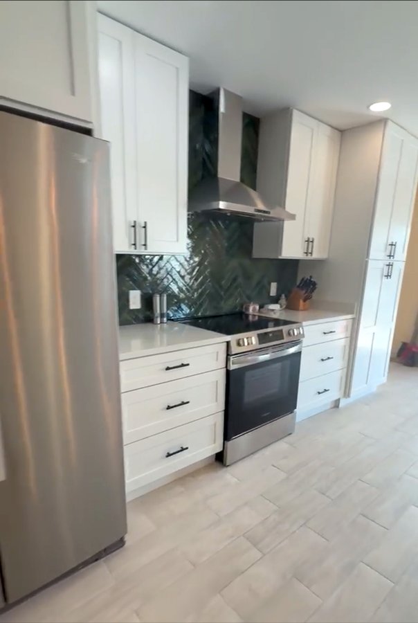 Finished kitchen with white shaker cabinets, quartz countertops, and green herringbone tile backsplash in Panama City Beach