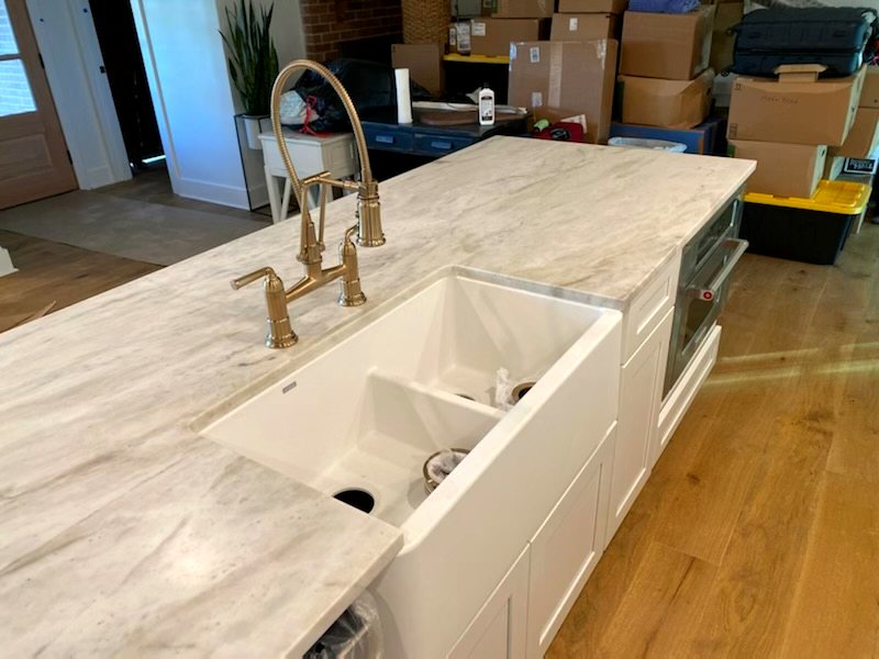 Kitchen island with marble countertop, farmhouse sink, and brass gooseneck faucet
